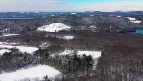 Aerial-footage-flying-high-over-a-winter-landscape-in-Maine-with-forest,-fields,-and-lakes