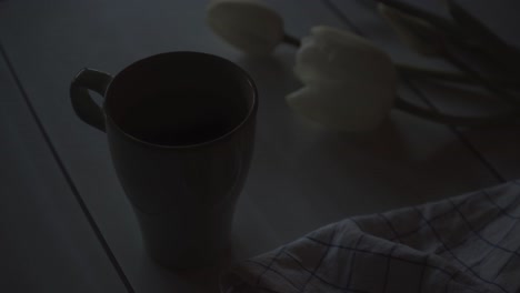 sun rising in early morning illuminating fresh cup of tea and white tulip flowers on table, close up view