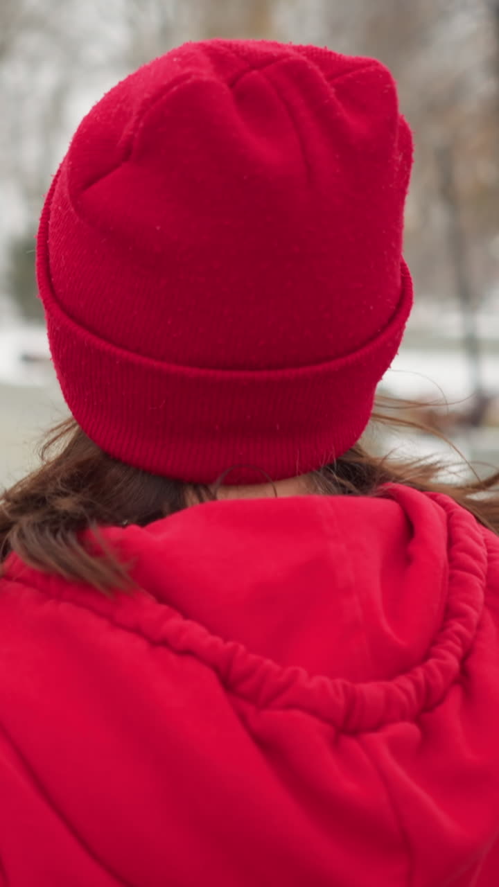 close up of woman jogging along snowy park pathway in red hoodie and black leggings surrounded by serene benches bushes iron railing lamp posts distant cross monument conveying cold fitness motion