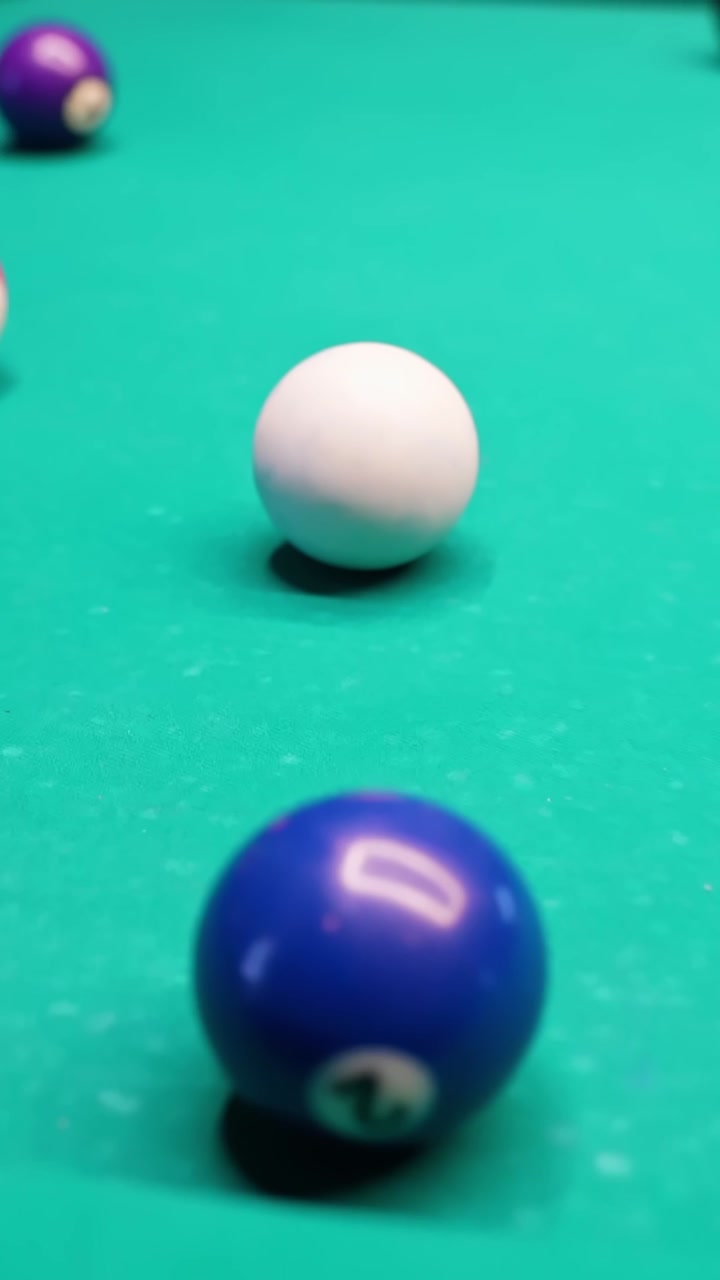 Vertical close-up of cue ball and blue 2 on green pool table felt with shallow depth of field, ideal for sports bar promos, game night ads, and cinematic b-roll.