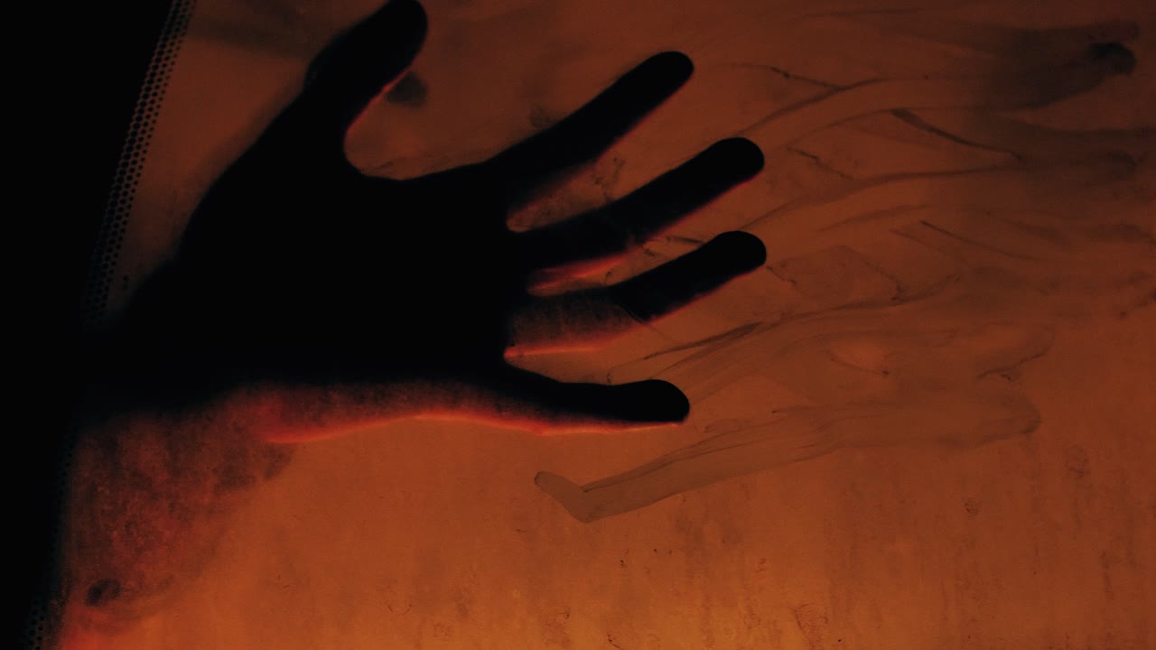 Immagine intensa di una silhouette di mano che preme contro un finestrino d'auto illuminato, evocando disperazione e un senso di fine.
