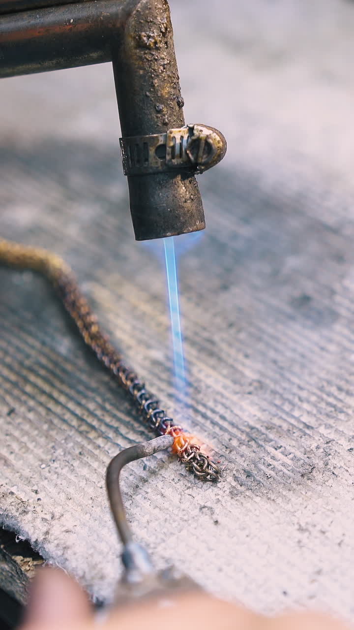 CU: skilled jeweler connects links of decorative chain with special welding tools on fireproof asbestos cover close view