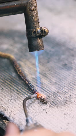 cu: skilled jeweler connects links of decorative chain with special welding tools on fireproof asbestos cover close view