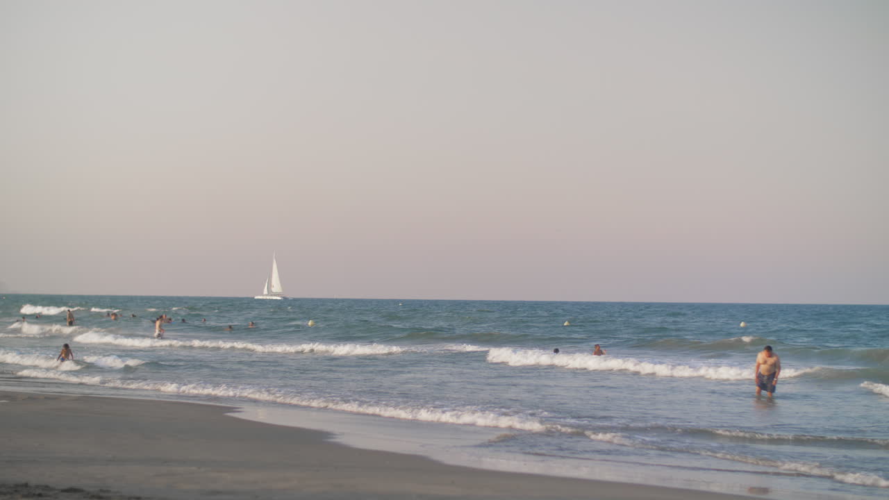 vista del mar con personas bañándose y velero blanco