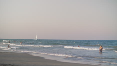 Sea-view-with-people-bathing-and-white-sailboat