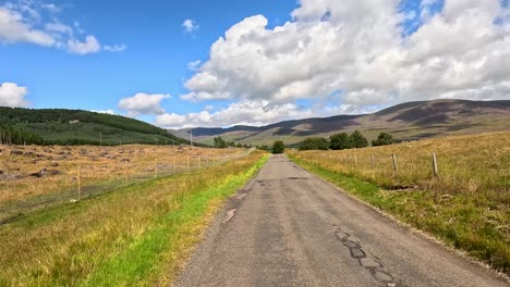 a vehicle travels a narrow country road through scenic scottish hills under bright daylight, with gentle camera movement and expansive landscape views