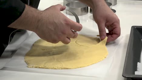 in a modern kitchen, hands press a metal cutter into rolled-out cookie dough. the baker skillfully shapes the dough, preparing for baking. enjoy the processes of cookie preparation.