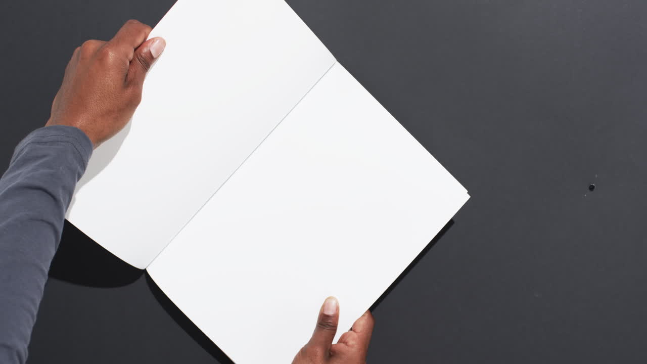 Video of hand of african american man holding book with blank pages, copy space on black background