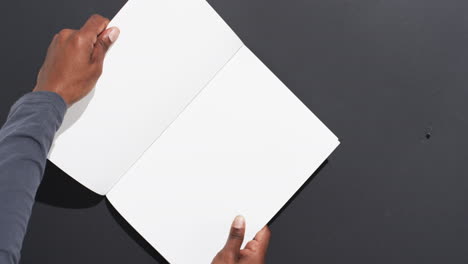 video of hand of african american man holding book with blank pages, copy space on black background