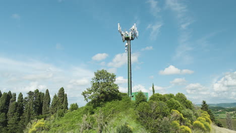 torre de telecomunicaciones con antenas en medio de árboles verdes en la colina contra el cielo soleado en italia