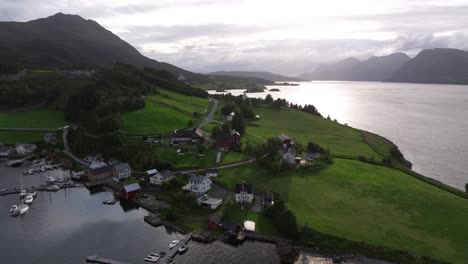 cloud diffuses light cast over grassy hillside with quaint european village built up above lakeshore with boats