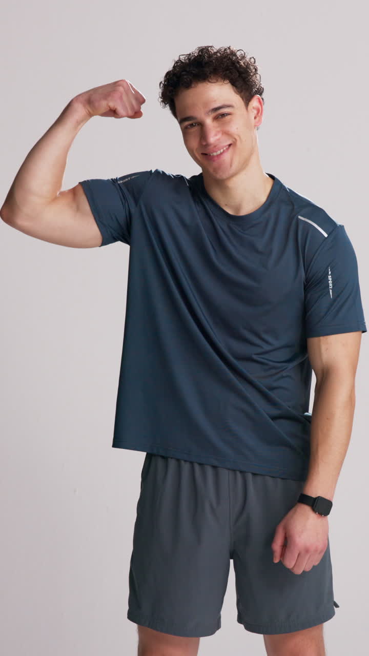 Confident Young Man Flexing Bicep and Smiling in Studio