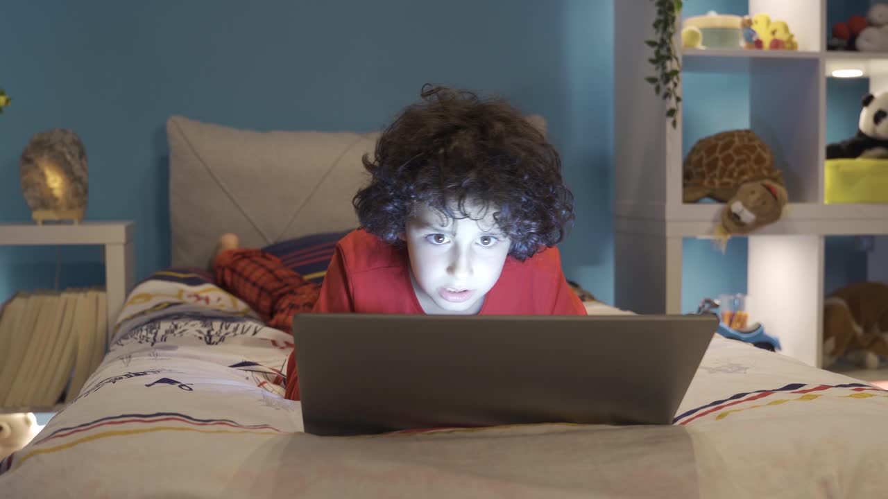 un niño adicto a los juegos jugando en su computadora portátil por la noche en su habitación.