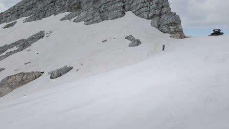 drone shot of a woman skiing from top of the mountain kanin downhill n white snowy slopes, sky covered with grey clouds in background visible some other nearby mountains