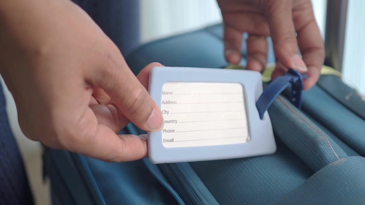 Person Attaching Identification Tag to Travel Suitcase