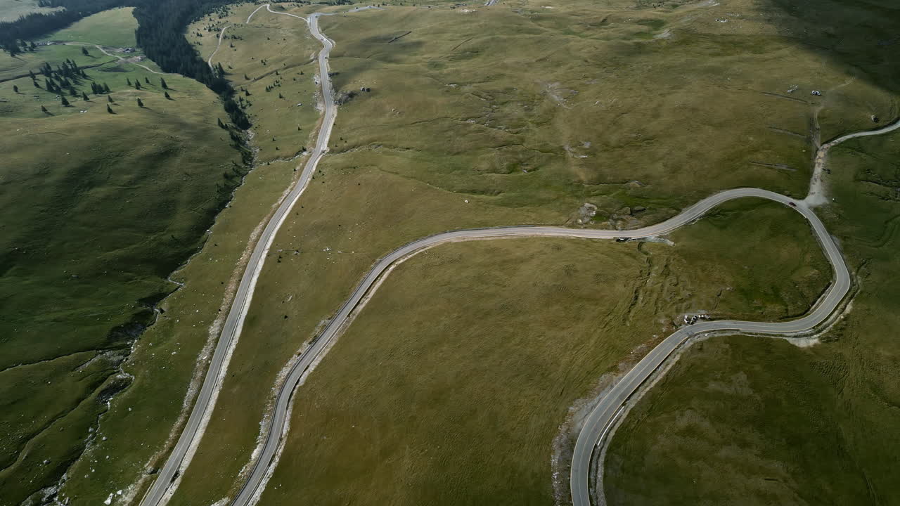 una serena vista de arriba hacia abajo de la carretera transalpina en rumania, con gracia sinuosa en medio de exuberantes prados verdes, interrumpidos por árboles y características sutiles del terreno
