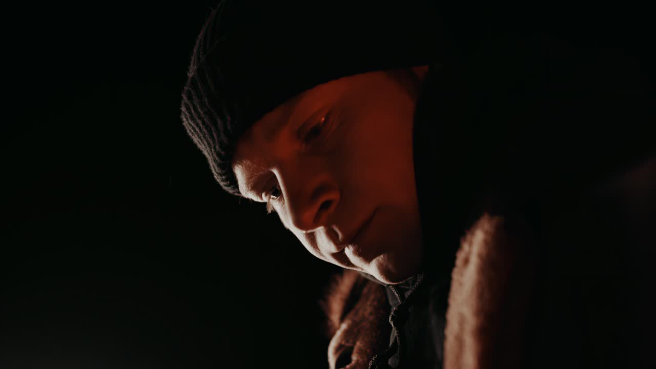 캠프 불 커피: 캠프 불 에 앉아있는 젊은 노숙자 남자가 후드를 곧게 할 때 입술 사이에 담배 필터를 들고 있습니다.