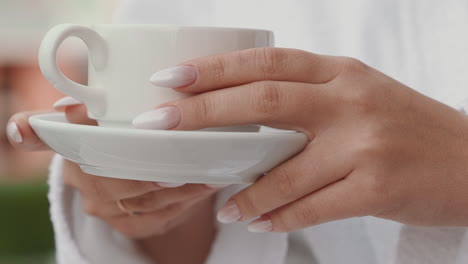 lady with elegant manicure in bathrobe holds cup of coffee