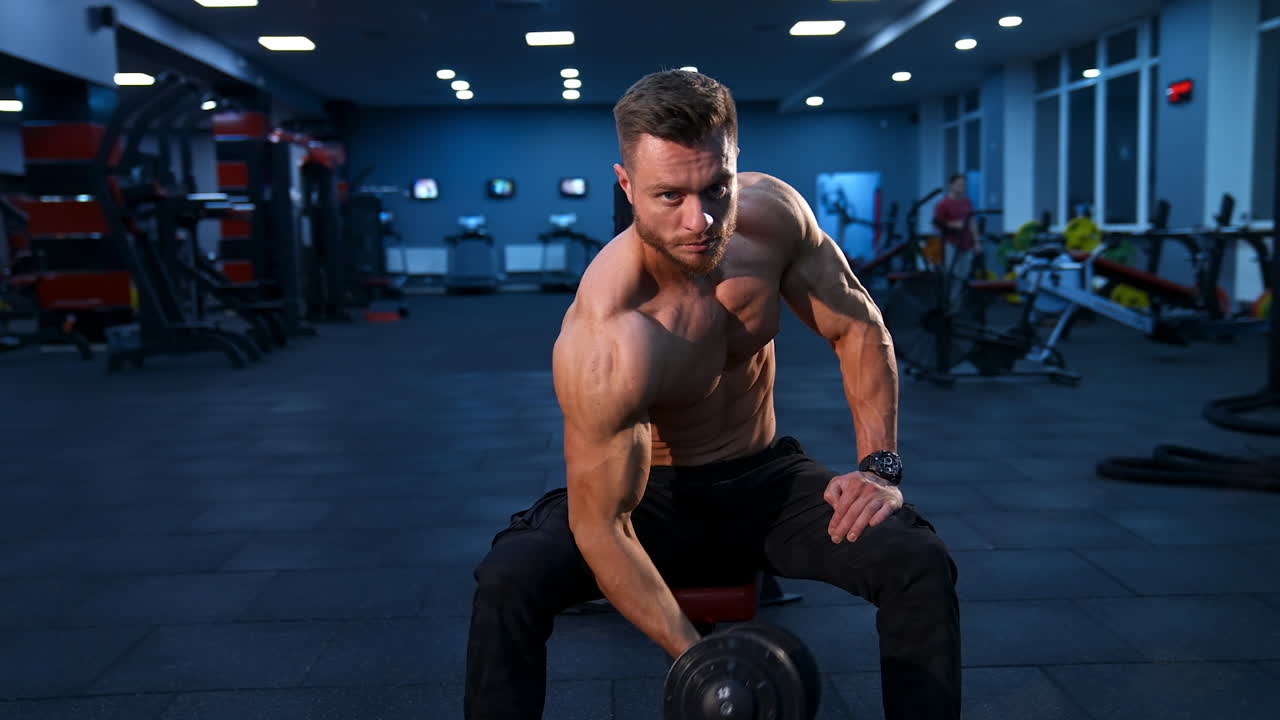 Power fitness man biceps. Handsome sportsman exercising with dumbbell while sitting in gym