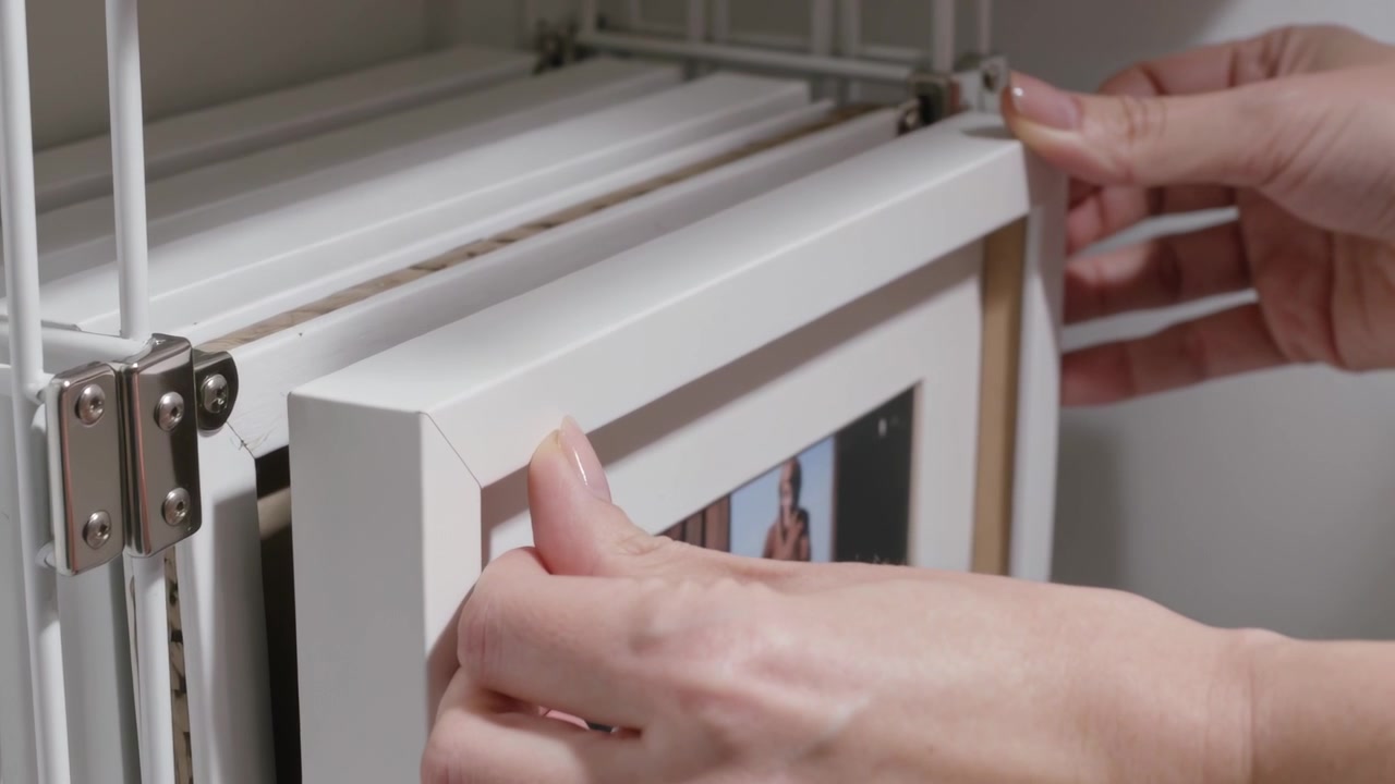 Mani curate afferrano il bordo e fanno scivolare una cornice bianca in una rastrelliera metallica, allineandola per la conservazione.