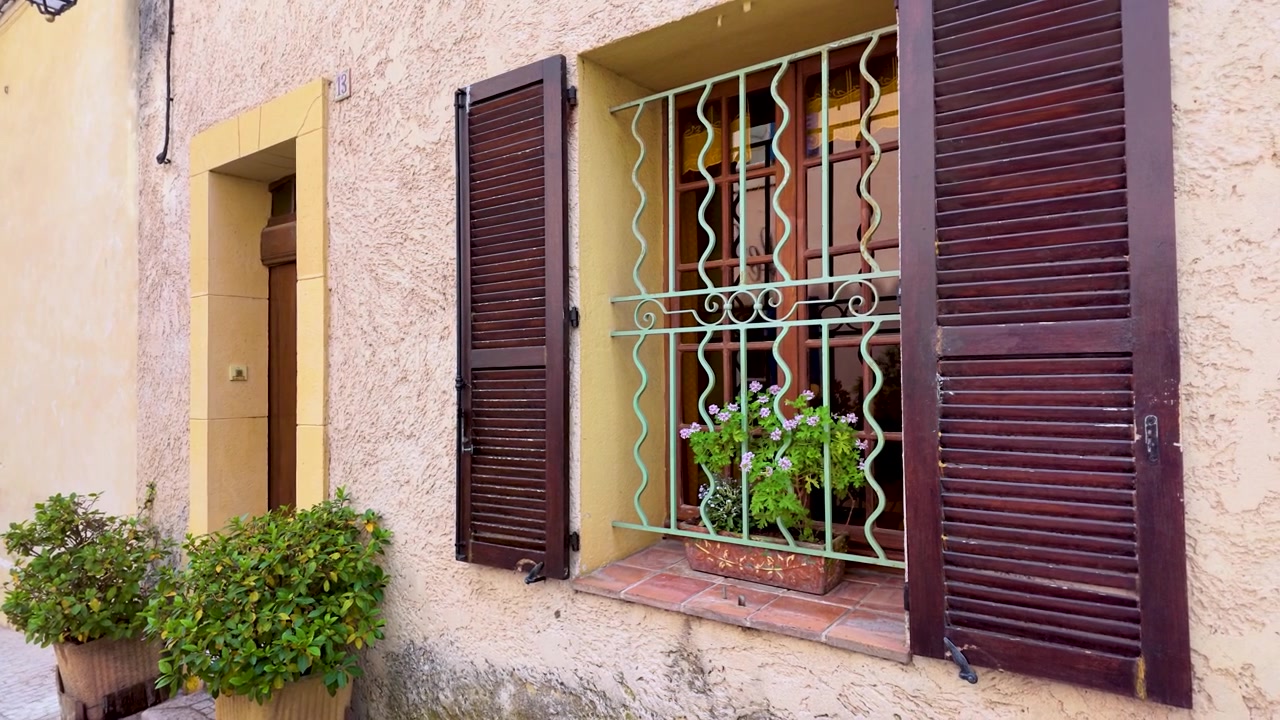 Zoom lento verso una finestra rustica con persiane marroni e fiori in Provenza, Francia