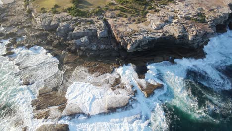 Bird's-Eye-View-Of-Ocean-Waves-Breaking-On-Coastal-Cliffs-In-Summer---Clovelly-Beach---Eastern-Suburb,-Sydney,-NSW,-Australia