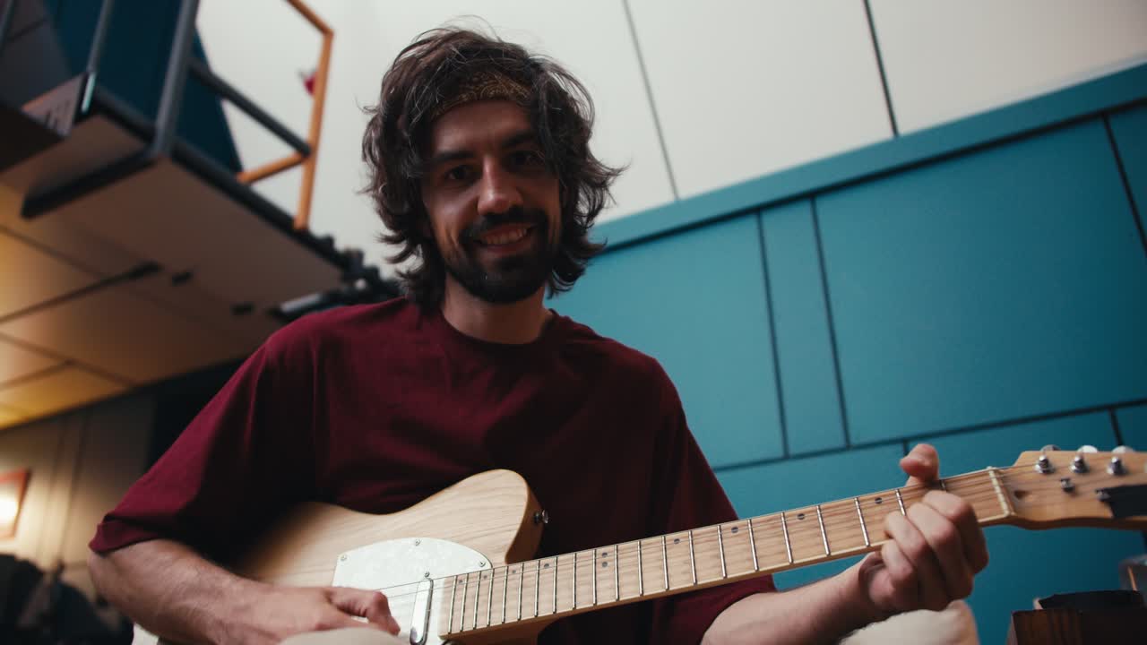un hombre con cabello peludo con barba en una camiseta roja toca la guitarra eléctrica y mira a la cámara