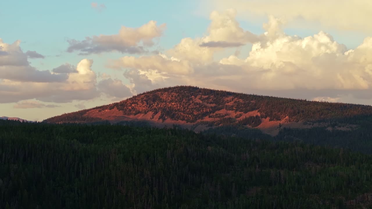 Ampia ripresa aerea di un altopiano nella foresta nazionale di Uinta-Wasatch-Cache, Utah, al tramonto, con montagne illuminate di rosso, pini e un cielo estivo azzurro