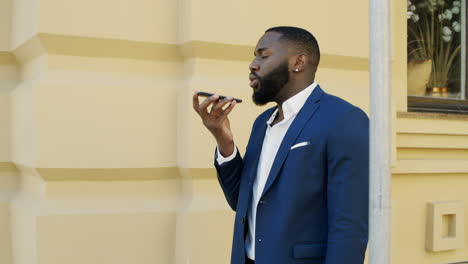 Focused-african-businessman-using-speakerphone-outside.-Afro-man-walking-outdoor