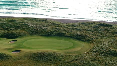 aerial orbit around golf green with flagstick blowing in the wind on stunning blue coast in northern ireland