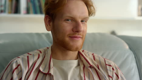 feliz hipster descansando en el sofá en casa de cerca. hombre rojo sonriente apoyado en el sofá