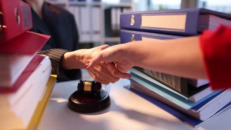 people shaking hands over a table with a gavel and legal binders