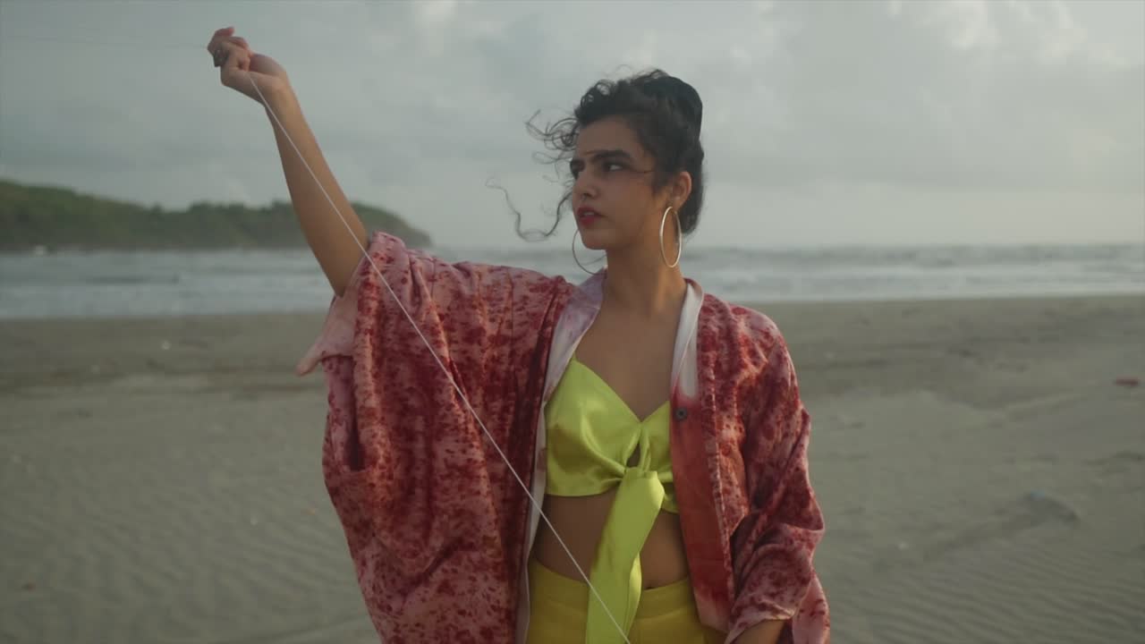 A beautifully captured view showcases a stunning Asian model, gracefully gazing at a kite against the backdrop of a breathtaking beachside scenery