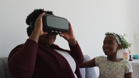 African-american-garndmother-using-vr-headset-sitting-on-the-couch-at-home