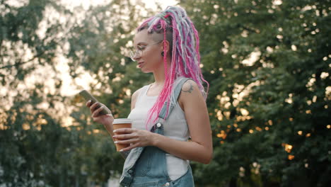 woman with pink dreadlocks using phone in park