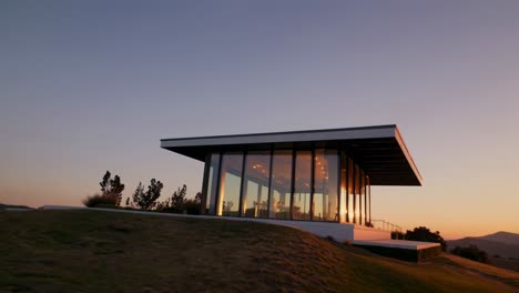 sun setting behind a modern glass house built on a hilltop, reflecting the warm colors of the evening sky, creating a peaceful and idyllic scene