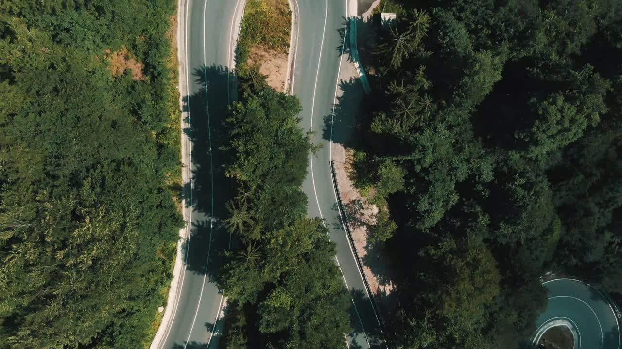 Toma aérea en 4K de coches circulando por una carretera con curvas en la ladera de una montaña