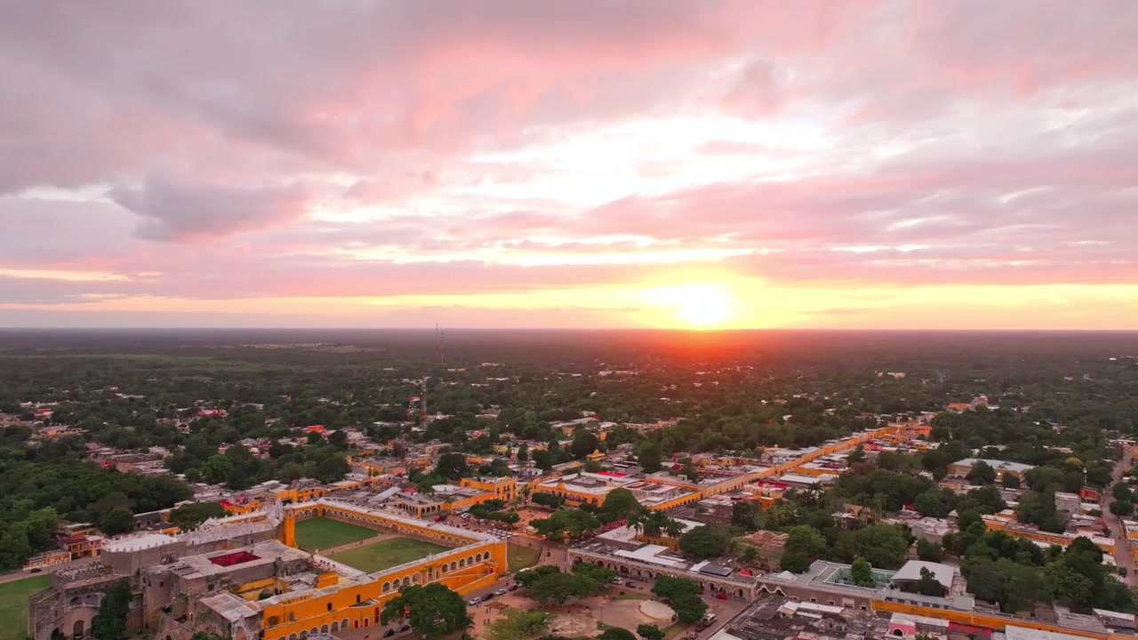Panorama aéreo sobre Izamal, Yucatán, México, ao crepúsculo, com uma suave luz rosada do anoitecer espalhando-se pelos telhados coloniais e pela floresta tropical