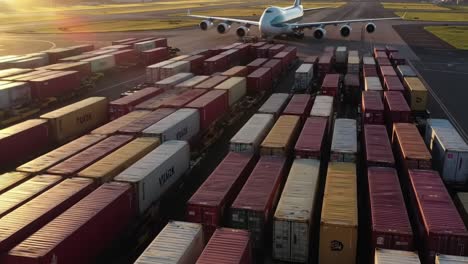 an enormous airplane is positioned on the runway, surrounded by a sea of colorful shipping containers at a bustling transportation hub as the sun sets, casting a warm glow over the scene.