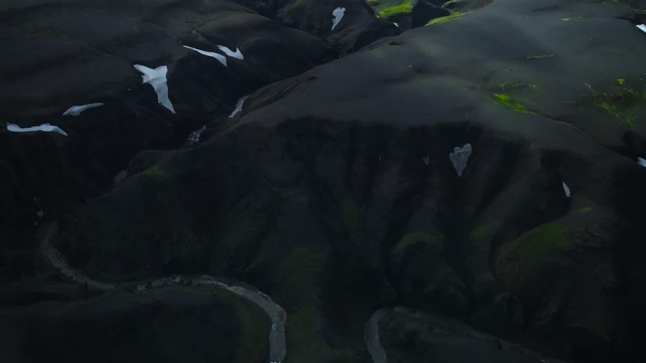 Aerial drone footage slowly rising up and revealing gorgeous Iceland or Greenland nature landscape with mountains covered in moss and white snow and deep cliffs that are steep and black with shadows.