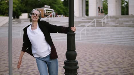 una chica feliz y despreocupada con ropa casual y elegante está girando, bailando alrededor de un pilar en la calle. sonriente, joven alegre