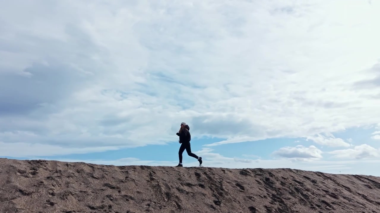 Running along the sandy ridge under a cloudy sky near the beach during the afternoon