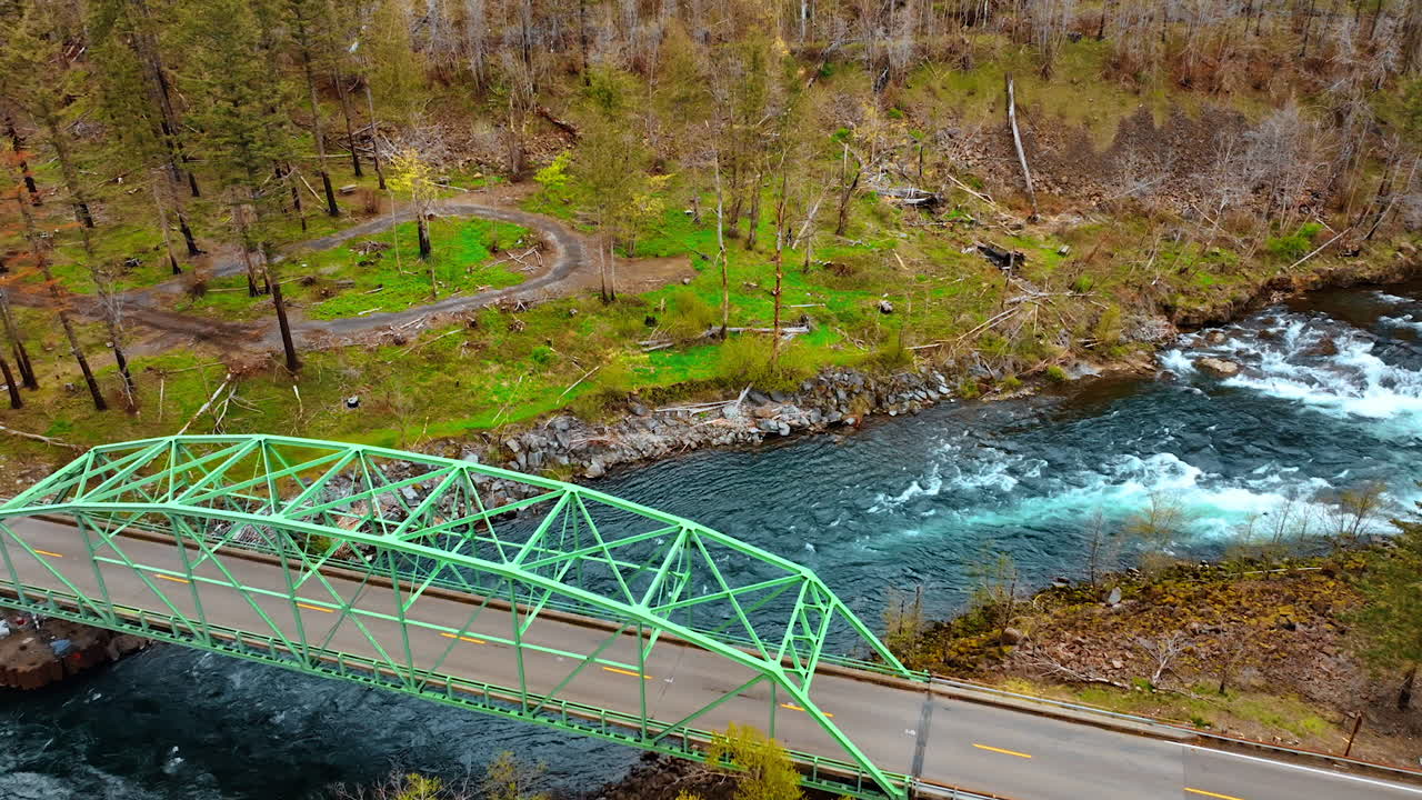 Car bridge over the narrow mountainous river with car crossing it. Drone footage above the river with rapids.