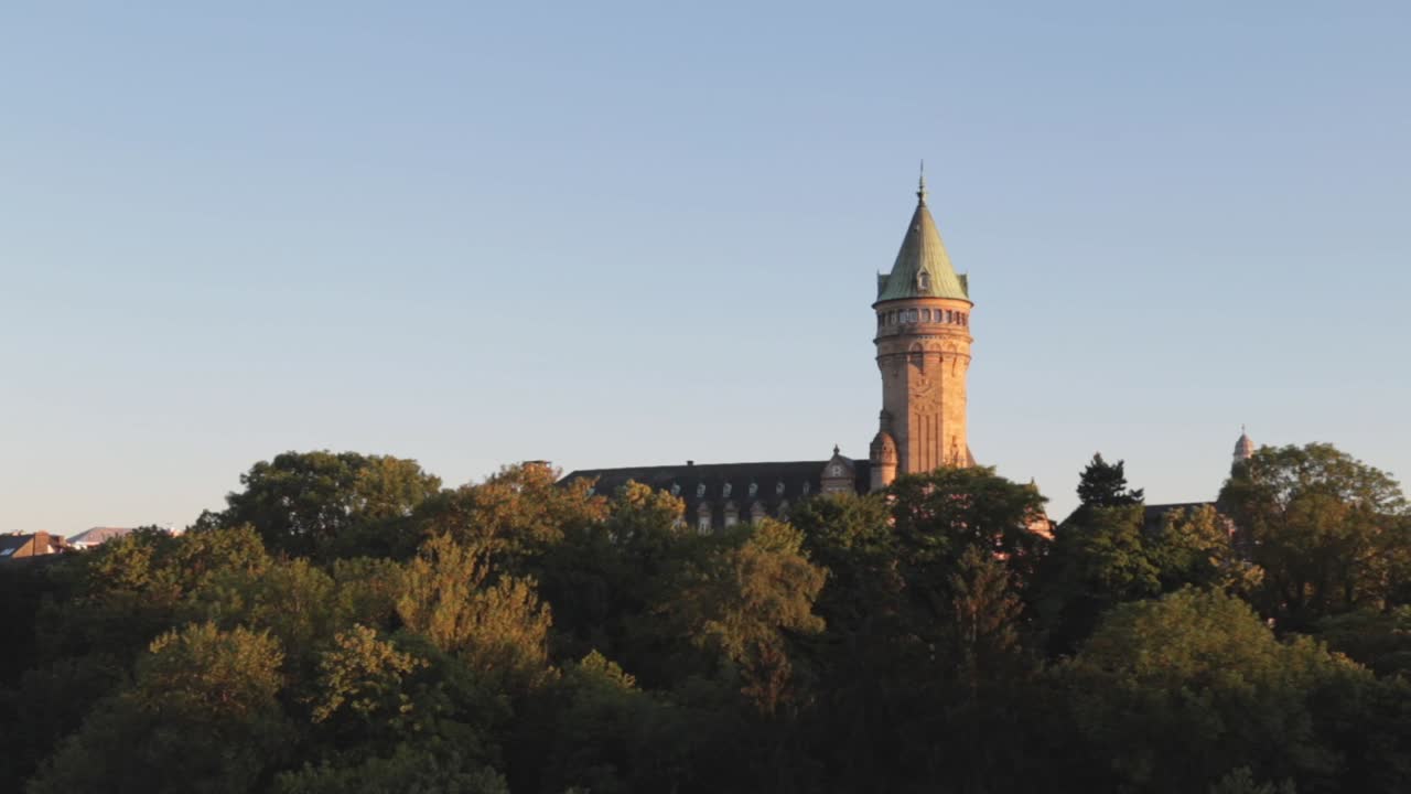 Clock tower towering over trees in Luxembourg City at sunset on a summer day