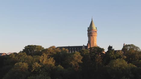 uhrturm, der bei sonnenuntergang an einem sommertag über bäumen in der stadt luxemburg thront