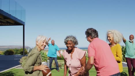 Happy-senior-diverse-people-playing-rugby-in-garden-at-retirement-home