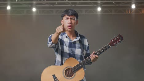adolescente asiático con guitarra gritando a la cámara mientras está de pie en el escenario