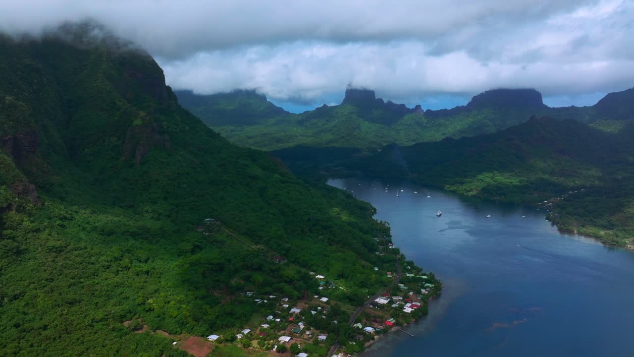 Monte Rotui e Baia di Opunohu a Moorea, Polinesia Francese, vista aerea con drone di lussureggianti creste verdi tropicali che scendono verso le calme acque della baia sotto un soffitto di nuvole basse, con movimento di panoramica ascendente in avanti.