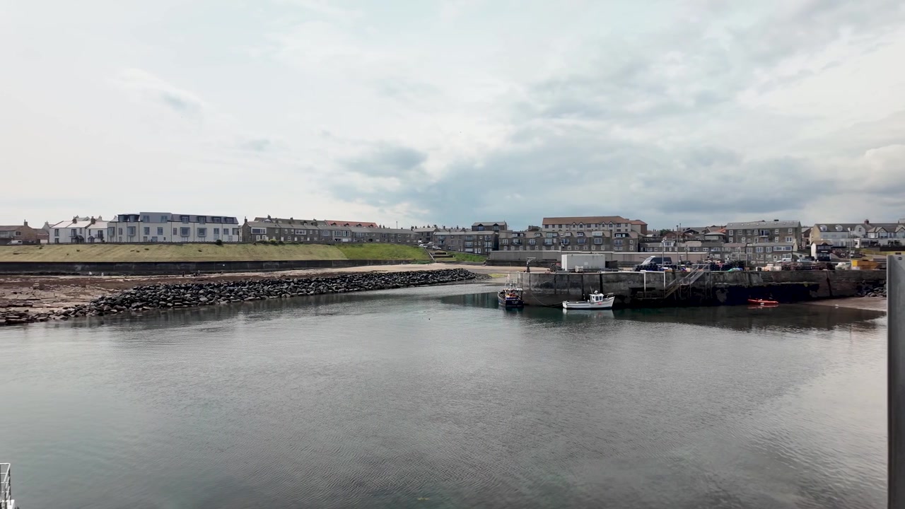 Vista panorámica del puerto de North Sunderland en Seahouses, un encantador pueblo costero con barcos y edificios bajo un cielo nublado.