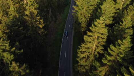 Drohnenaufnahme-Eines-Sportwagens,-Der-Im-Sommer-In-Einem-Grünen-Wald-Die-Straße-Entlang-Fährt